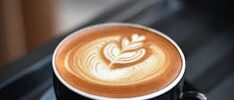 A beautifully crafted cappuccino with intricate latte art in a black ceramic mug on a dark surface.
