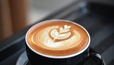 A beautifully crafted cappuccino with intricate latte art in a black ceramic mug on a dark surface.