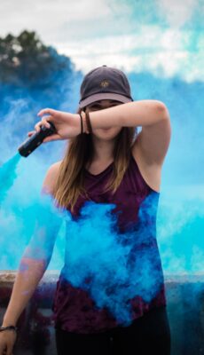 A stylish woman surrounded by bright blue smoke outdoors, creating a dynamic fashion statement.