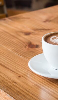 Close-up of a white cup of latte with artistic foam on a rustic wooden table.