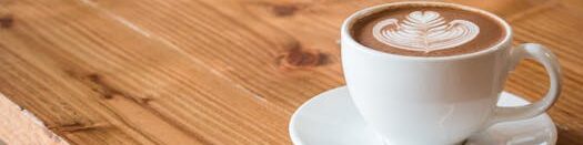 Close-up of a white cup of latte with artistic foam on a rustic wooden table.