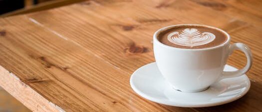 Close-up of a white cup of latte with artistic foam on a rustic wooden table.
