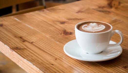 Close-up of a white cup of latte with artistic foam on a rustic wooden table.